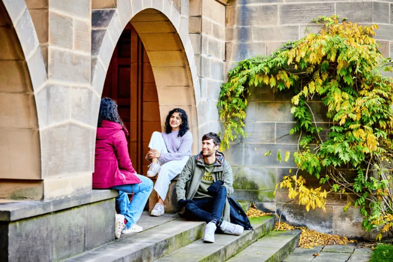 Three students sat on stone steps underneath an archway