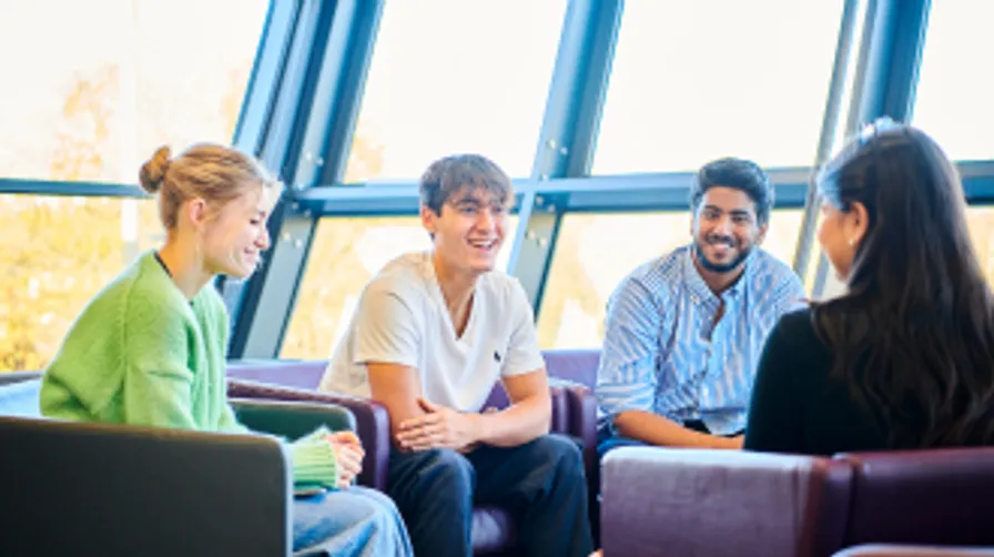 A mixed group of students sat in comfy chairs chatting
