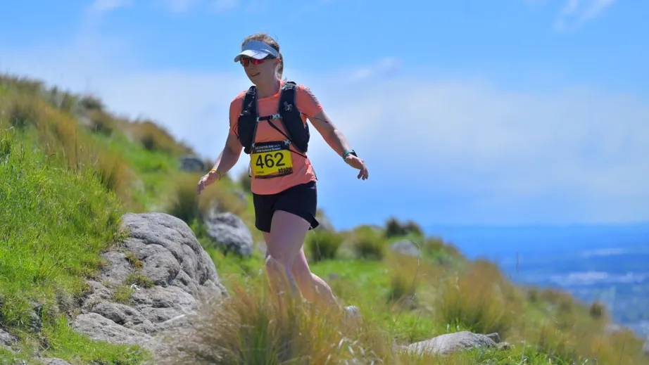 A women running on a grassy hillside in the sunshine with the sea in the background