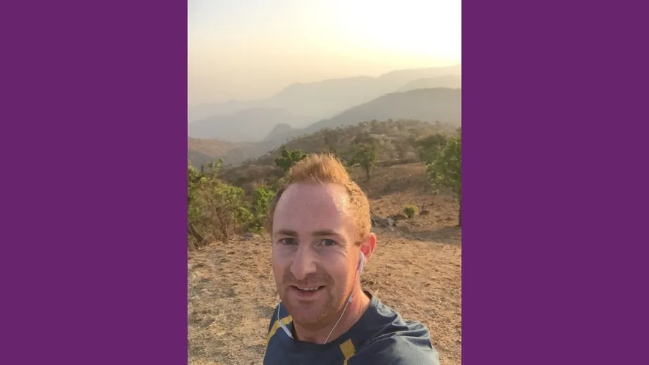 A red haired man in running gear taking a selfie with a range of hills behind him