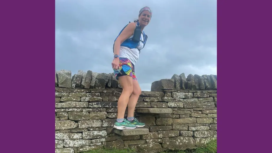 A women perched on top of a drystone wall wearing running gear