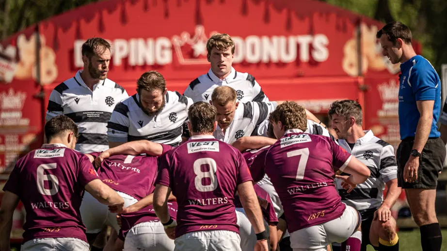Two teams of rugby players wearing purple tops, and black and white tops, playing against each other