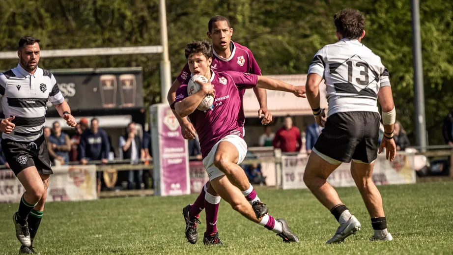 Two teams of rugby players wearing purple tops, and black and white tops, playing against each other