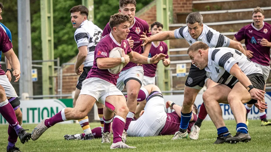 Two teams of rugby players wearing purple tops, and black and white tops, playing against each other