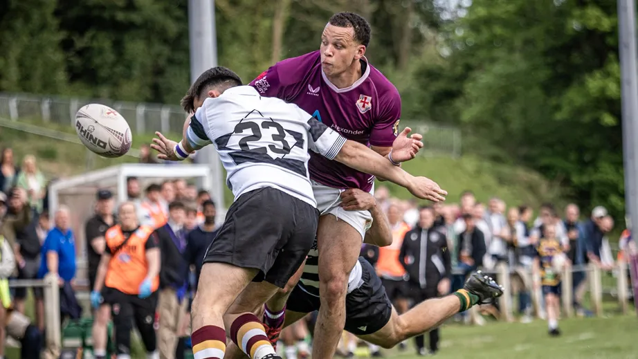 Two rugby players wearing purple tops, and black and white tops, playing against each other