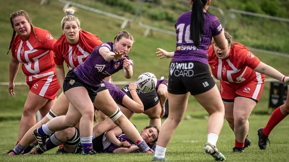 Two teams of female rugby players wearing purple tops, and red and white tops, playing against each other