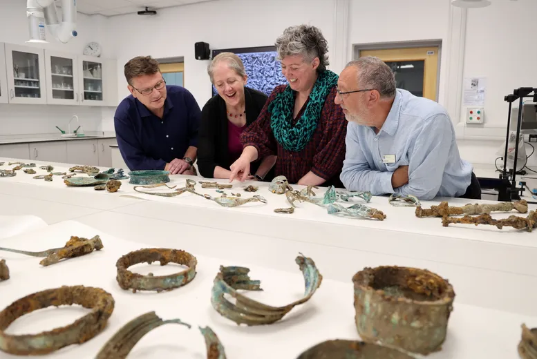 The Melsonby Hoard team stood talking to each other next to a white table where a number of Iron Age artefacts are laid out.