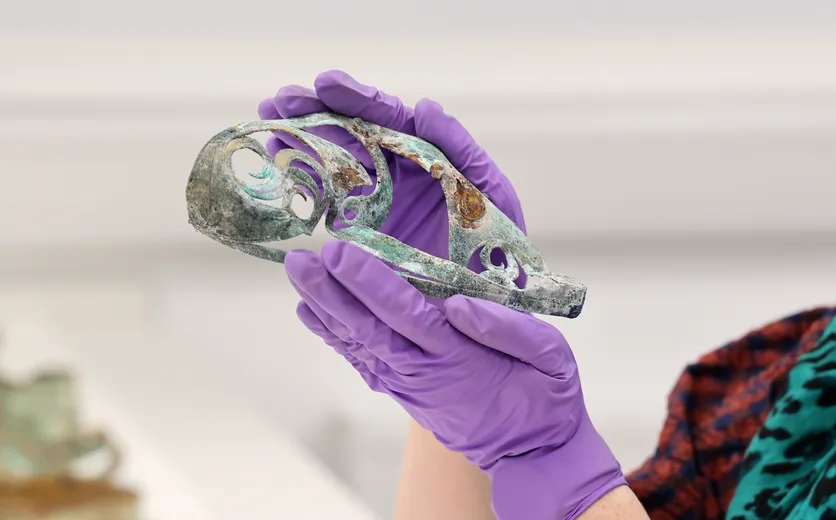 A fragment of decorative Iron Age metalwork, being held by someone wearing purple gloves to avoid damaging it.