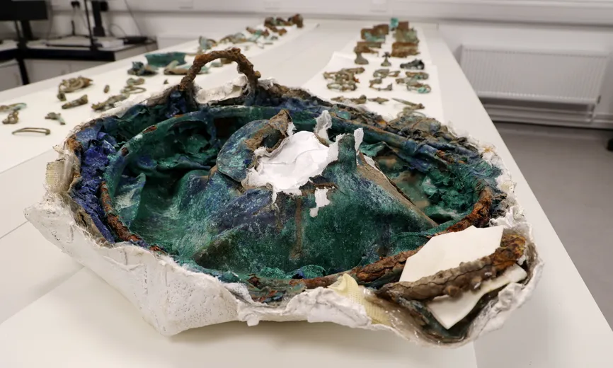 An Iron Age cauldron displayed on a white table, with a large hole in the centre where it has been crushed.