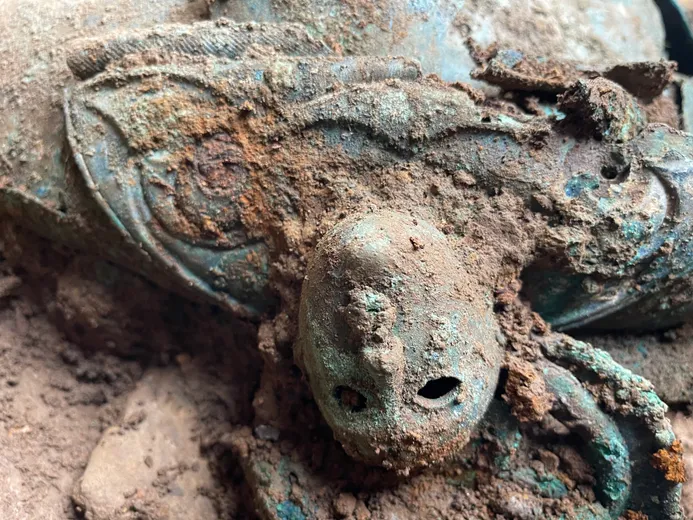 A close-up of one of the two mask-like human faces decorating a lidded vessel excavated from the Melsonby Hoard
