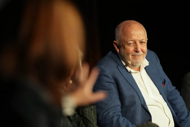 Man sitting smiling facing camera, blurred woman in foreground