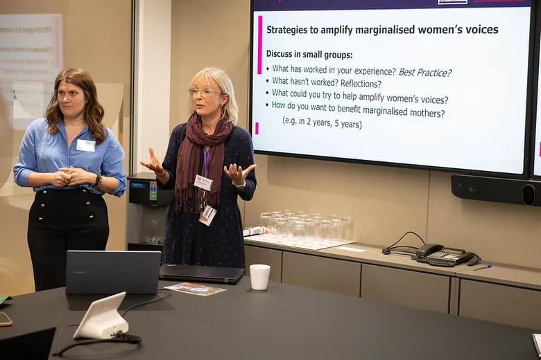 Two woman standing speaking, with a PowerPoint slide visible