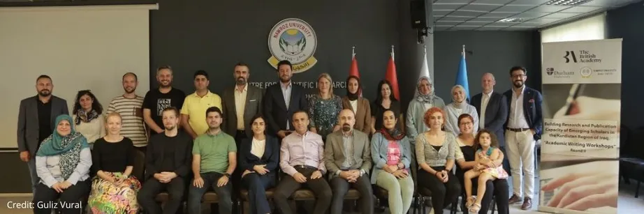 A group of people sitting and standing and looking at the camera.