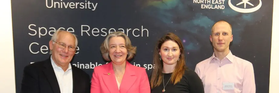 A group of people standing in front of a banner which says space research. They are smiling at the camera.