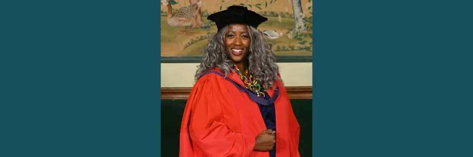 Anne-Marie Imafidon wearing a black academic cap and red robes smiling at the camera.