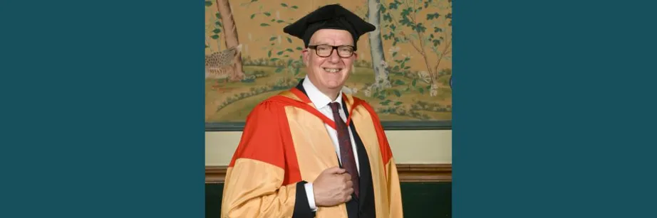 Richard Ovenden wearing a black academic cap and red and gold robes smiling at the camera