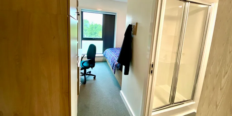 A picture of an en-suite room taken from the entrance. Pictured are a desk and chair, and a doorway to a toilet and shower.