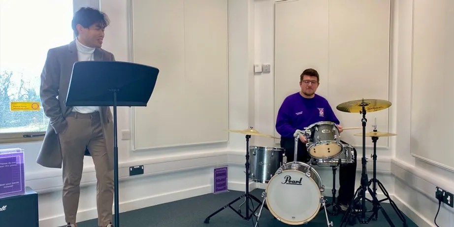 Two students using the music room, one singing and the other playing drums